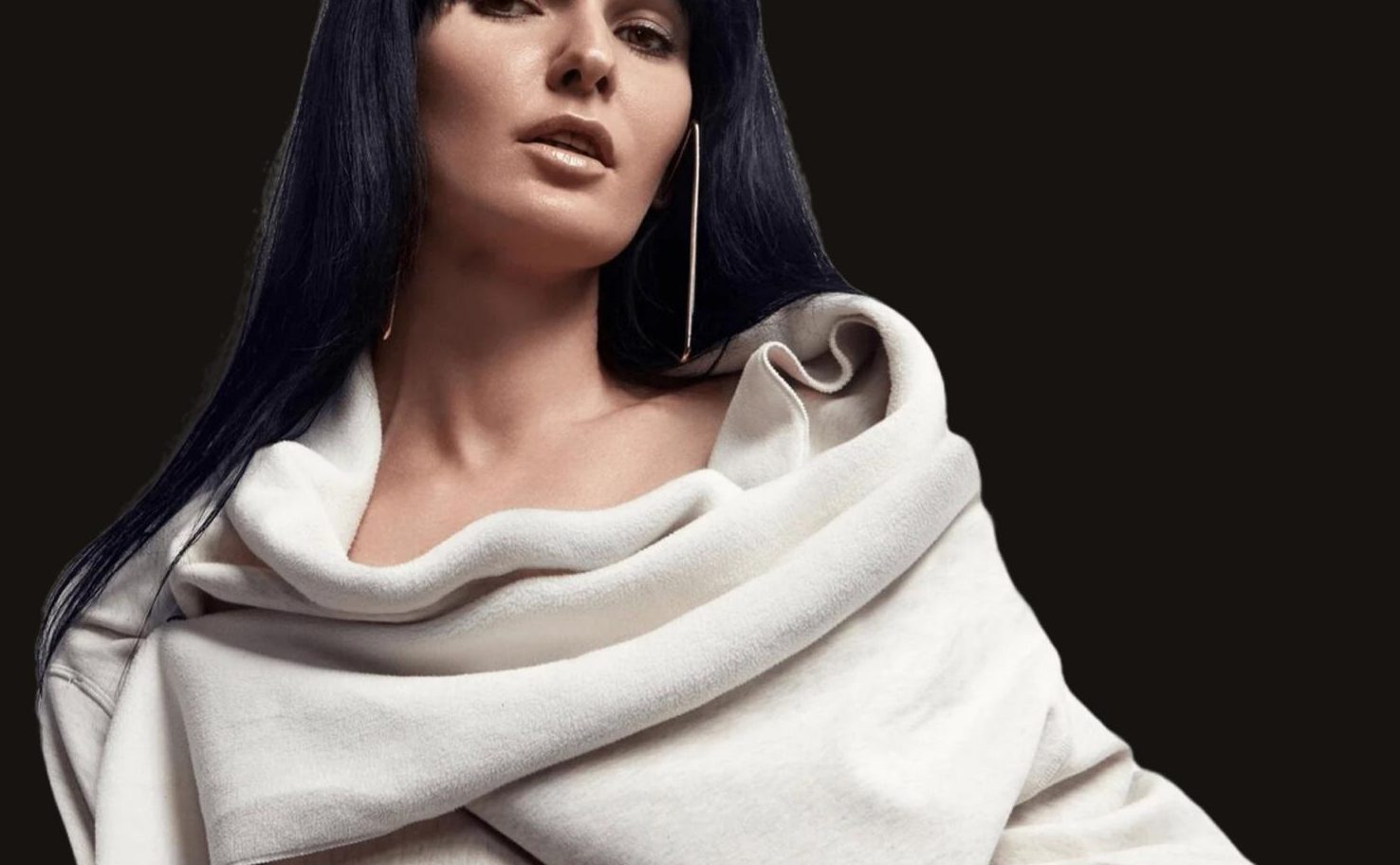Model wearing a long sleek black Veloura wig with a cream shawl